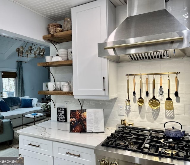 kitchen with light stone counters, tasteful backsplash, range hood, and white cabinets