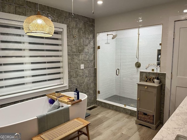 bathroom with independent shower and bath, hardwood / wood-style floors, and tile walls