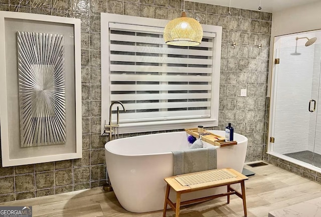 bathroom featuring wood-type flooring, separate shower and tub, and tile walls