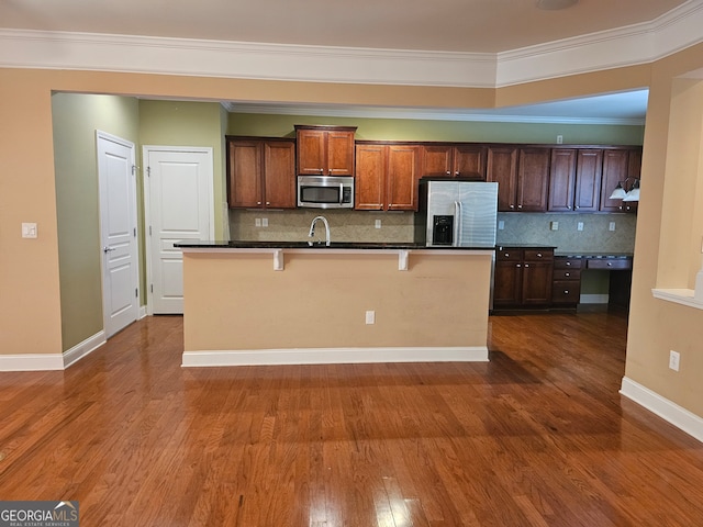 kitchen with a kitchen breakfast bar, a center island with sink, stainless steel appliances, dark hardwood / wood-style floors, and ornamental molding