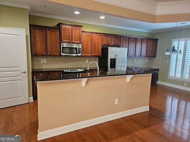 kitchen with a kitchen island with sink, dark wood-type flooring, ornamental molding, appliances with stainless steel finishes, and a kitchen bar