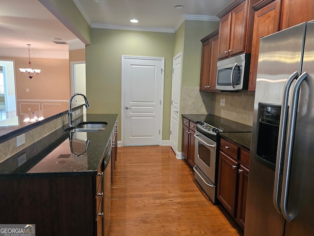 kitchen with sink, stainless steel appliances, a notable chandelier, light hardwood / wood-style floors, and decorative backsplash