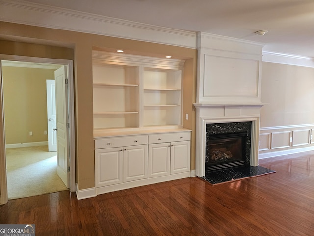 unfurnished living room with built in features, ornamental molding, a premium fireplace, and dark hardwood / wood-style flooring