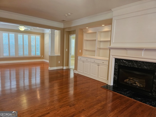 unfurnished living room with ceiling fan, a premium fireplace, decorative columns, ornamental molding, and hardwood / wood-style flooring