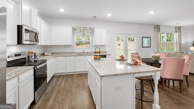 kitchen with stainless steel appliances, white cabinets, light wood-type flooring, and a healthy amount of sunlight