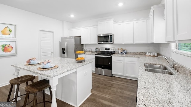 kitchen featuring light stone counters, white cabinets, sink, appliances with stainless steel finishes, and a breakfast bar area