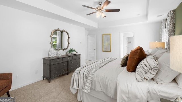 carpeted bedroom with a raised ceiling, ensuite bath, and ceiling fan