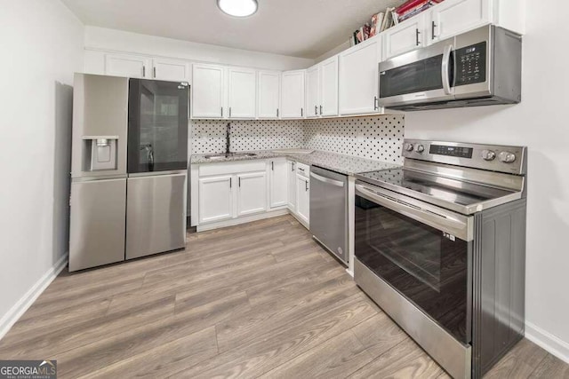 kitchen featuring white cabinets, sink, tasteful backsplash, stainless steel appliances, and light wood-type flooring