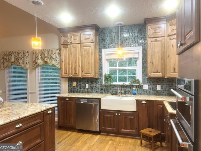 kitchen featuring decorative light fixtures, sink, backsplash, light hardwood / wood-style floors, and stainless steel appliances