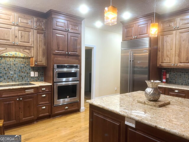 kitchen featuring decorative light fixtures, tasteful backsplash, light stone counters, stainless steel appliances, and light wood-type flooring