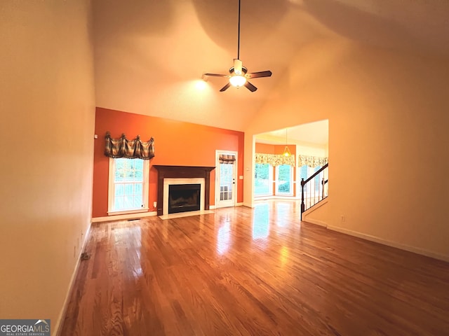 unfurnished living room featuring ceiling fan with notable chandelier, high vaulted ceiling, wood-type flooring, and a healthy amount of sunlight