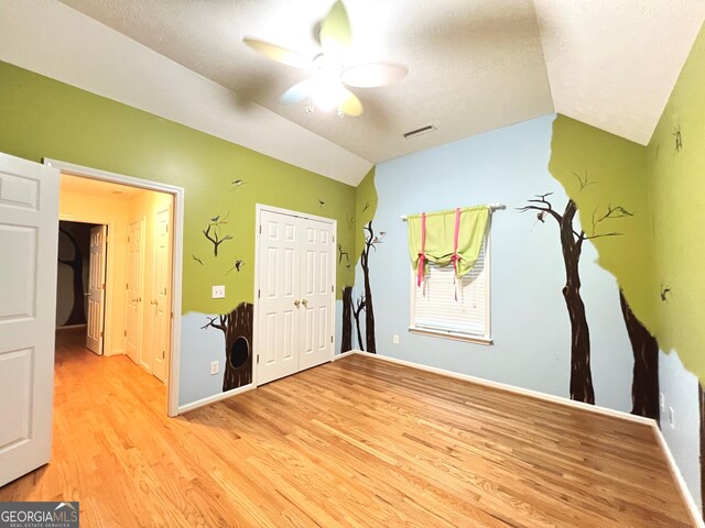 empty room featuring ceiling fan, light hardwood / wood-style floors, vaulted ceiling, and a textured ceiling