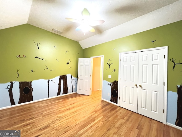 unfurnished bedroom with lofted ceiling, ceiling fan, light hardwood / wood-style floors, a textured ceiling, and a closet