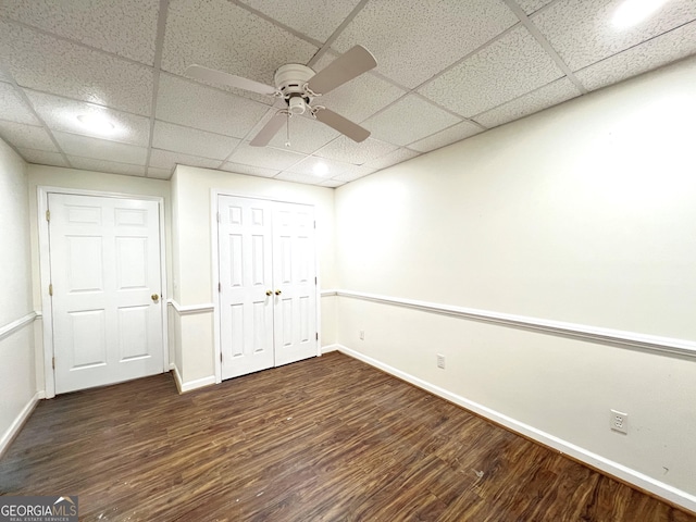 unfurnished bedroom featuring ceiling fan, a paneled ceiling, dark hardwood / wood-style flooring, and a closet