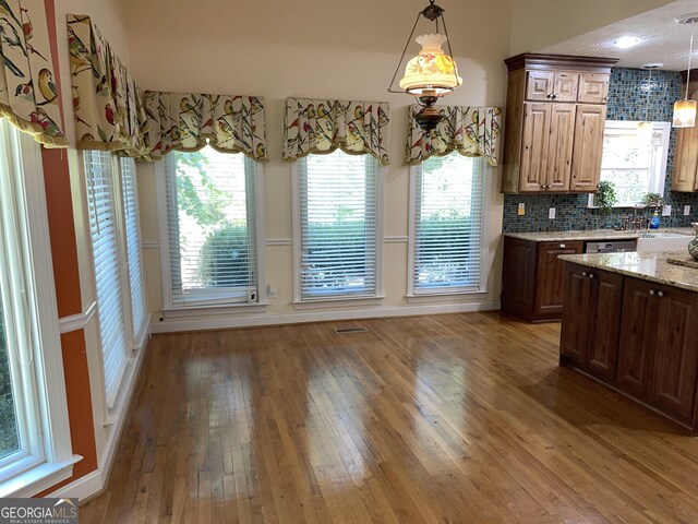 kitchen featuring dark hardwood / wood-style floors, decorative light fixtures, dishwasher, backsplash, and light stone counters