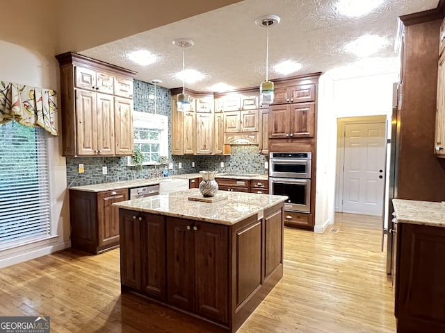 kitchen featuring pendant lighting, stainless steel appliances, a textured ceiling, a kitchen island, and light wood-type flooring