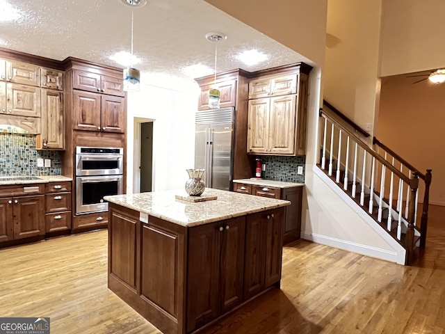 kitchen with a kitchen island, stainless steel appliances, decorative light fixtures, and light hardwood / wood-style flooring