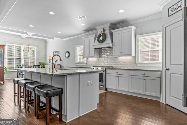 kitchen with sink, a kitchen island with sink, stone counters, stainless steel stove, and dark hardwood / wood-style floors