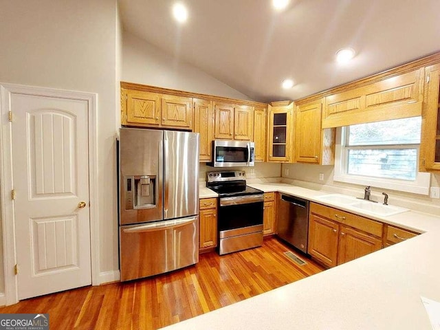 kitchen with appliances with stainless steel finishes, light wood-type flooring, vaulted ceiling, and sink