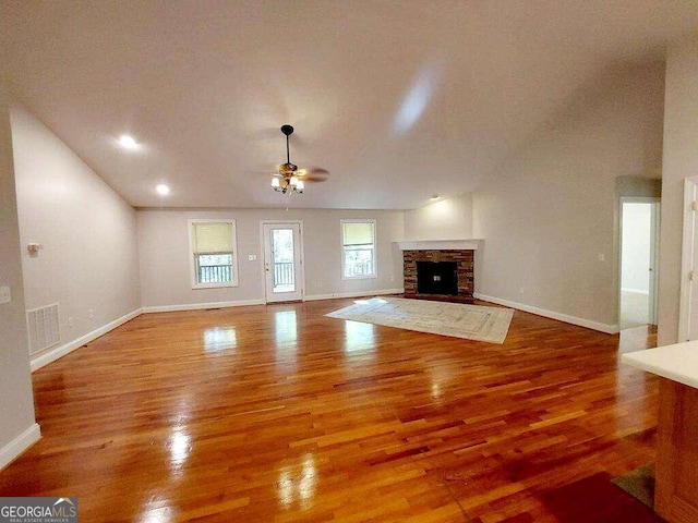 unfurnished living room with hardwood / wood-style flooring, ceiling fan, and a stone fireplace