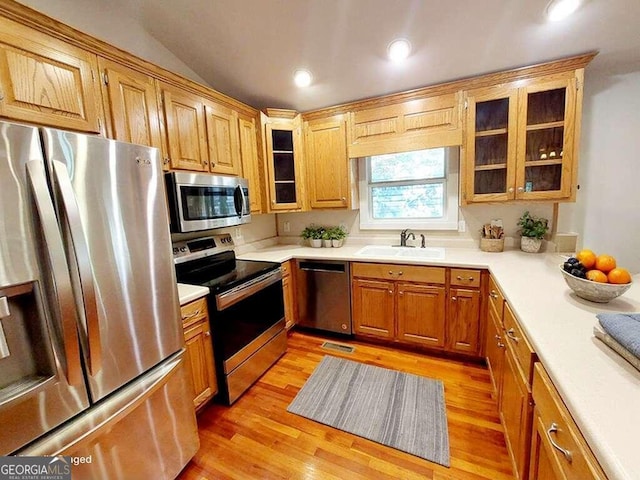 kitchen featuring appliances with stainless steel finishes, light wood-type flooring, lofted ceiling, and sink