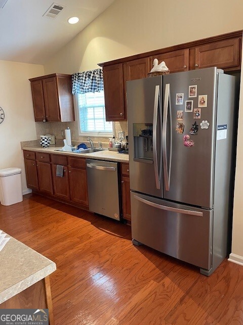 kitchen with sink, hardwood / wood-style flooring, backsplash, and appliances with stainless steel finishes