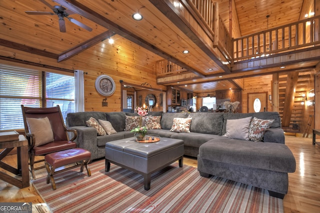 living room with light wood-type flooring, beam ceiling, wood walls, a high ceiling, and wooden ceiling