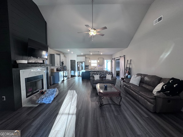 living room with a barn door, dark hardwood / wood-style flooring, a fireplace, high vaulted ceiling, and ceiling fan