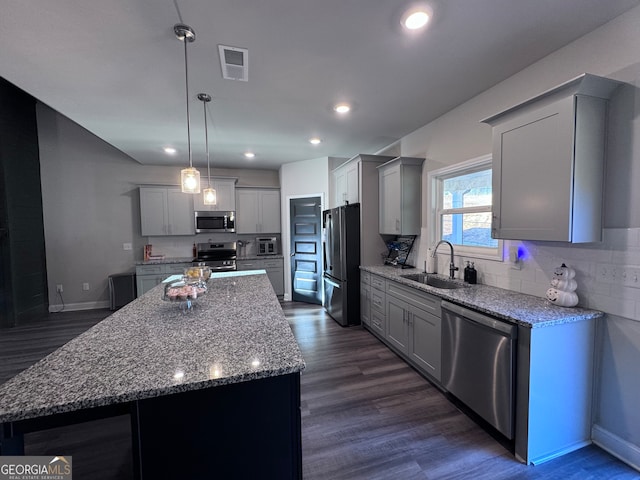 kitchen with hanging light fixtures, dark hardwood / wood-style flooring, appliances with stainless steel finishes, sink, and a center island