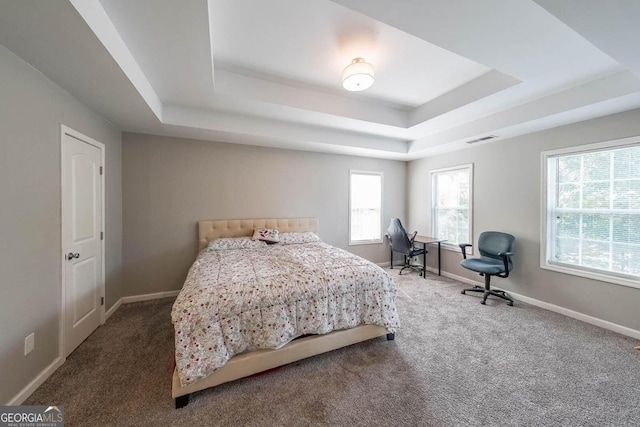 bedroom with carpet floors, a tray ceiling, and multiple windows