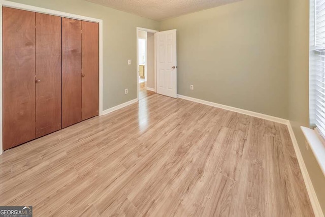 unfurnished bedroom featuring a textured ceiling, a closet, and light hardwood / wood-style flooring