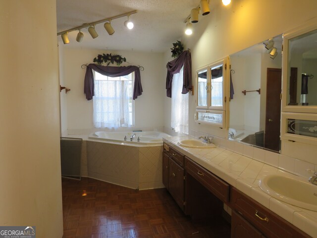 bathroom featuring tiled tub, track lighting, vanity, and a textured ceiling