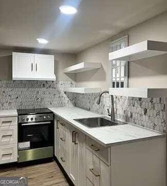 kitchen featuring stainless steel range with electric stovetop, decorative backsplash, sink, and white cabinets