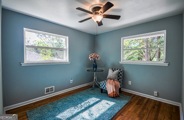 living area featuring ceiling fan, dark hardwood / wood-style floors, and a healthy amount of sunlight