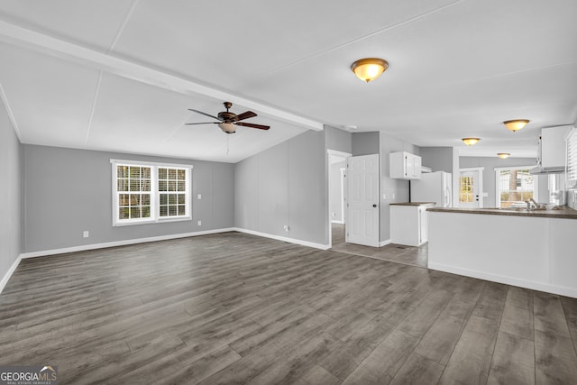 unfurnished living room featuring ceiling fan, lofted ceiling with beams, plenty of natural light, and dark wood-type flooring