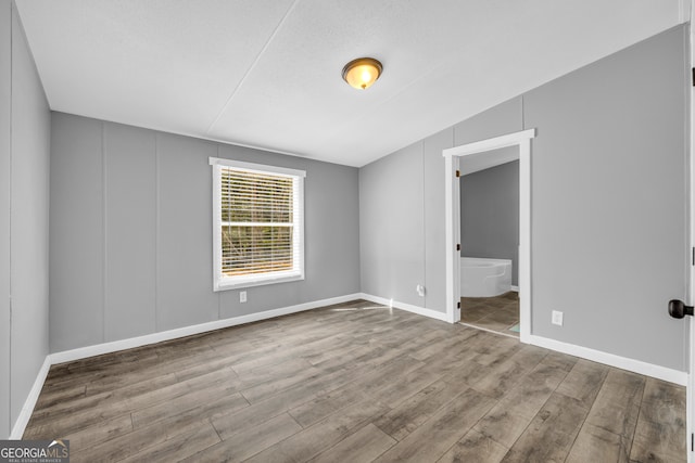 unfurnished bedroom featuring wood-type flooring, vaulted ceiling, connected bathroom, and a textured ceiling