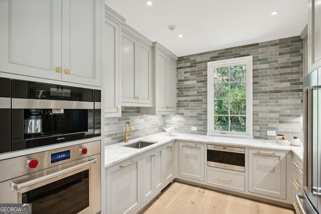 kitchen with light stone countertops, light wood-type flooring, tasteful backsplash, stainless steel appliances, and sink