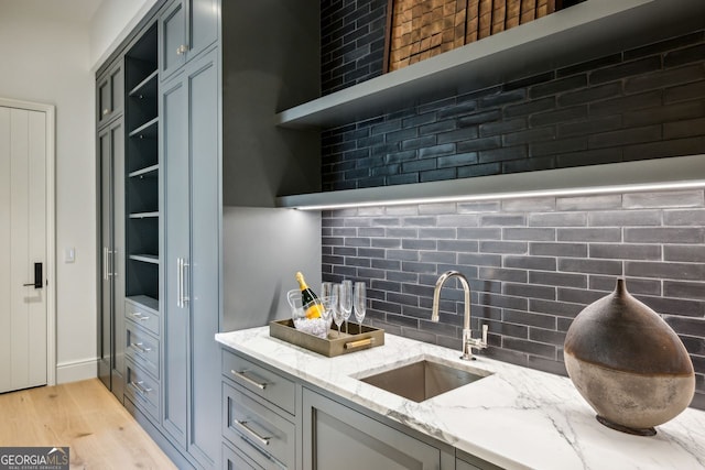 kitchen featuring decorative backsplash, light stone counters, sink, and light hardwood / wood-style flooring