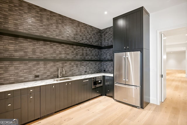 kitchen with light stone countertops, decorative backsplash, high end fridge, sink, and light hardwood / wood-style flooring