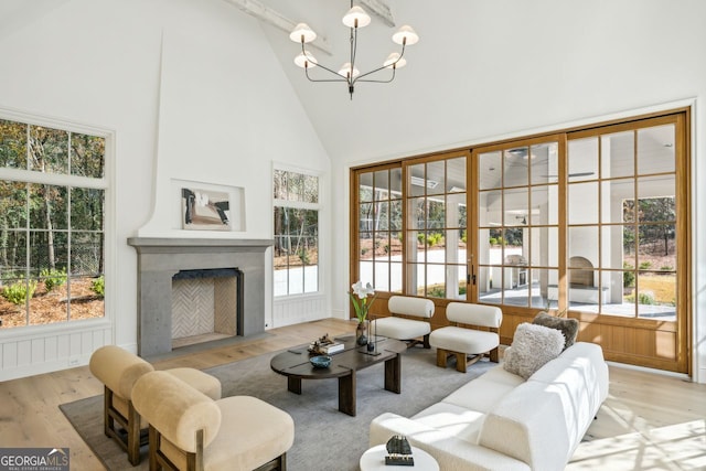 living room with high vaulted ceiling, a healthy amount of sunlight, a notable chandelier, and light wood-type flooring