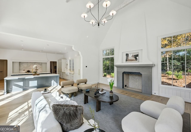 living room with a fireplace, light hardwood / wood-style flooring, high vaulted ceiling, and a chandelier