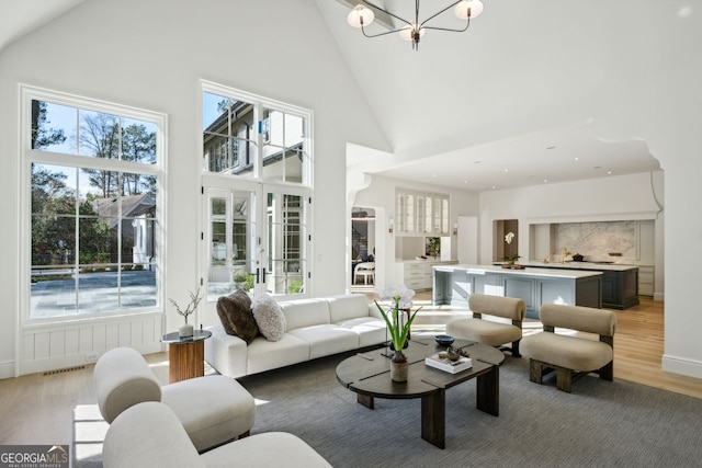 living room with a healthy amount of sunlight, light wood-type flooring, high vaulted ceiling, and a chandelier