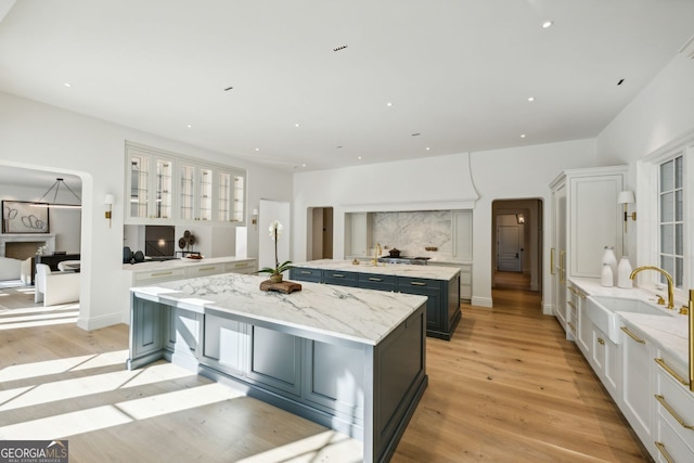 kitchen featuring white cabinetry, sink, light stone countertops, light hardwood / wood-style floors, and a kitchen island with sink