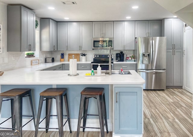 kitchen featuring gray cabinetry, kitchen peninsula, a kitchen breakfast bar, light hardwood / wood-style floors, and stainless steel appliances