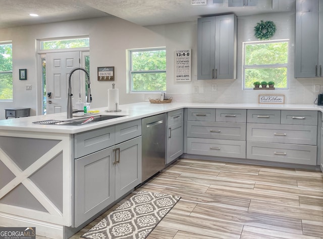 kitchen featuring a textured ceiling, stainless steel dishwasher, sink, and gray cabinetry