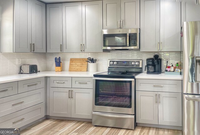 kitchen featuring gray cabinetry, light hardwood / wood-style floors, stainless steel appliances, and tasteful backsplash