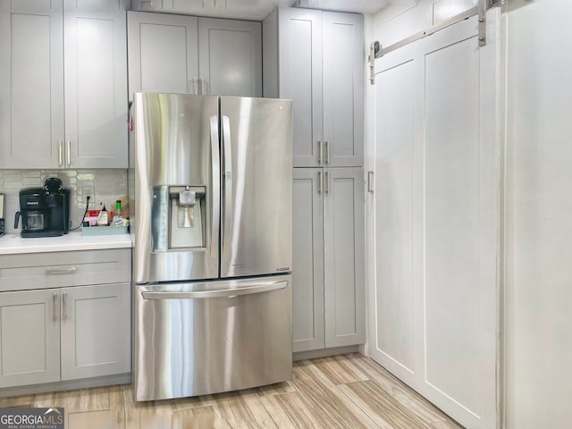 kitchen featuring light hardwood / wood-style flooring, gray cabinetry, stainless steel fridge with ice dispenser, a barn door, and tasteful backsplash