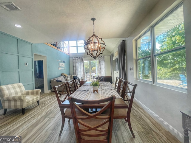 dining room with lofted ceiling, hardwood / wood-style floors, a textured ceiling, and an inviting chandelier