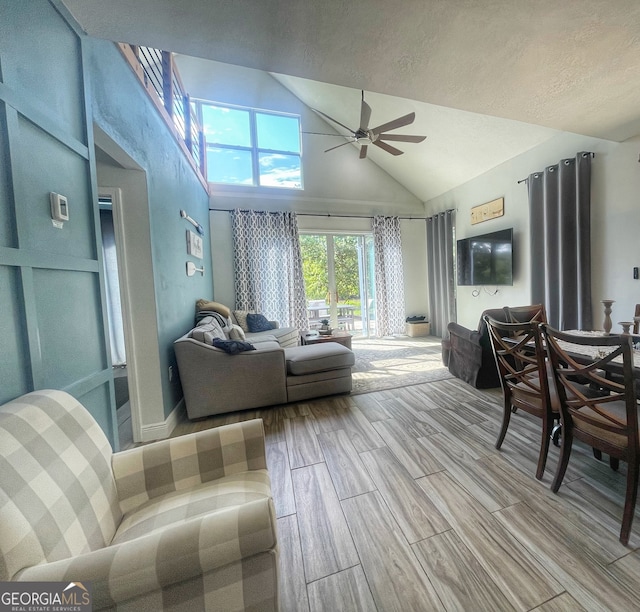 living room featuring a textured ceiling, high vaulted ceiling, light wood-type flooring, and ceiling fan