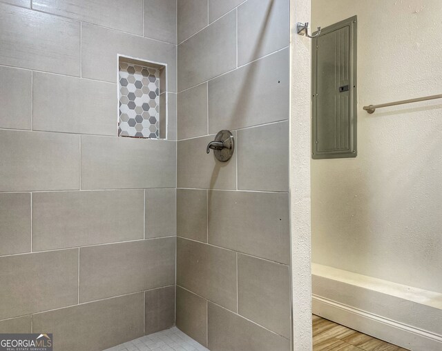 bathroom featuring a tile shower, hardwood / wood-style flooring, and electric panel